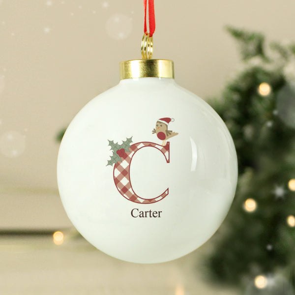 White Christmas ornament with letter 'C' and name 'Carter', featuring a Santa Claus design, against a blurred festive background.