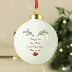 White Christmas ornament with reindeer antlers and text, hanging against a blurred festive background.
