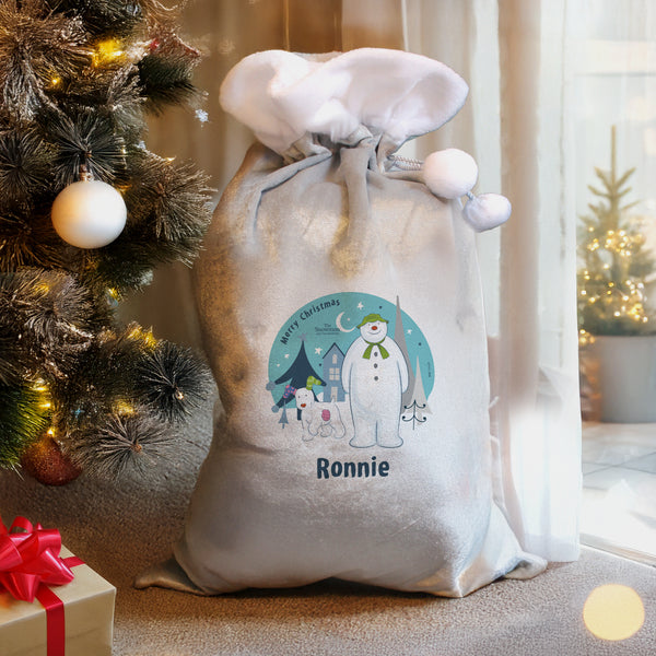 Personalized Christmas sack with a snowman design and the name 'Ronnie', placed next to a decorated Christmas tree.
