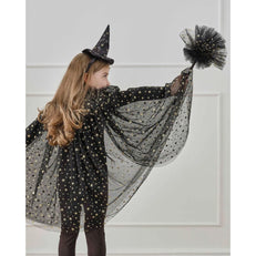 Child in a witch costume with a black hat and cape against a white wall